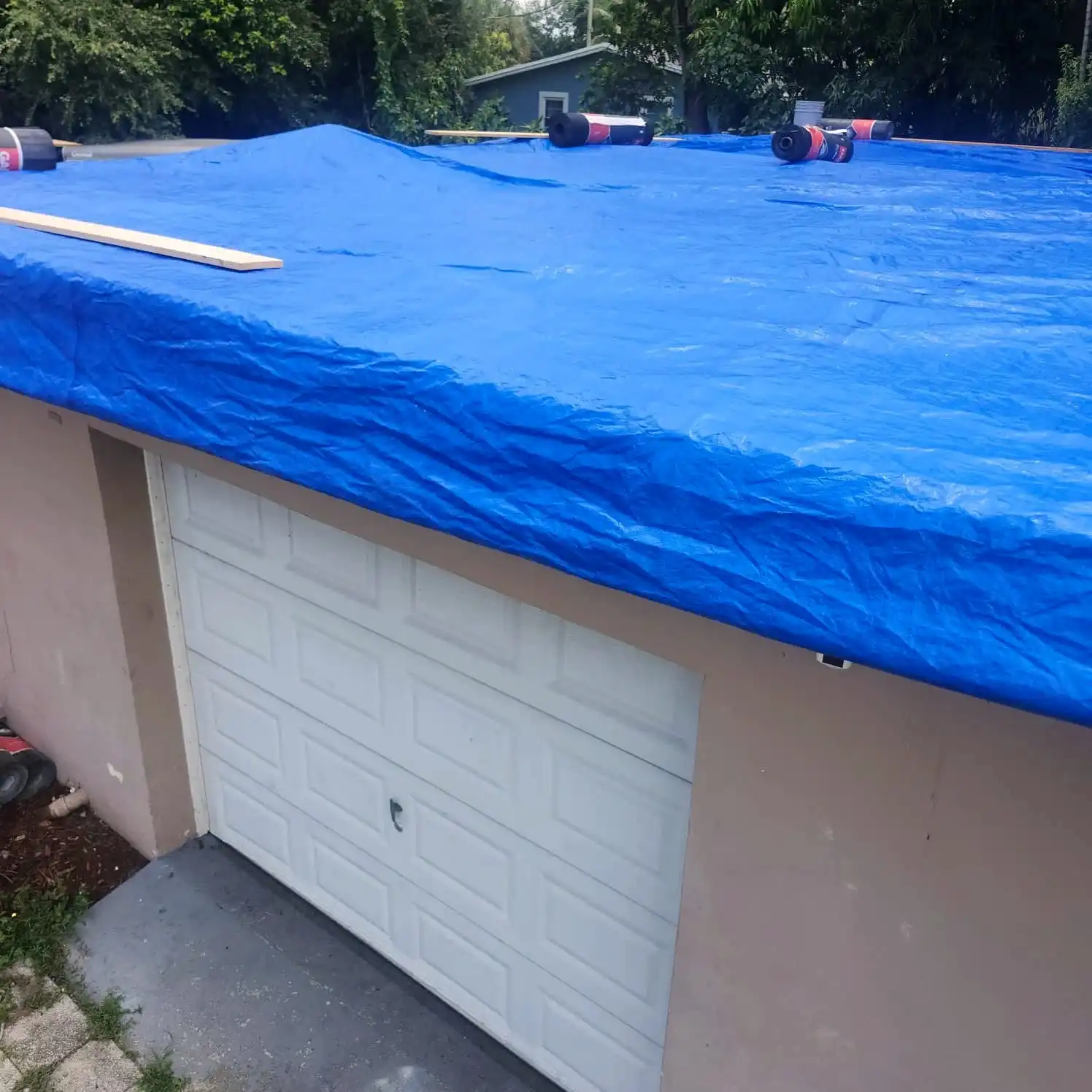 Blue tarp covering a roof over a garage, held down with boards